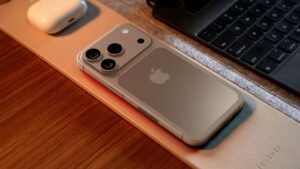 Overhead-view-of-an-iPhone-17-Pro-concept-lying-on-a-wooden-desk-next-to-a-laptop-and-AirPods-showing-its-potential-new-horizontal-camera-bar-design-and-Apple-logo.jpg
